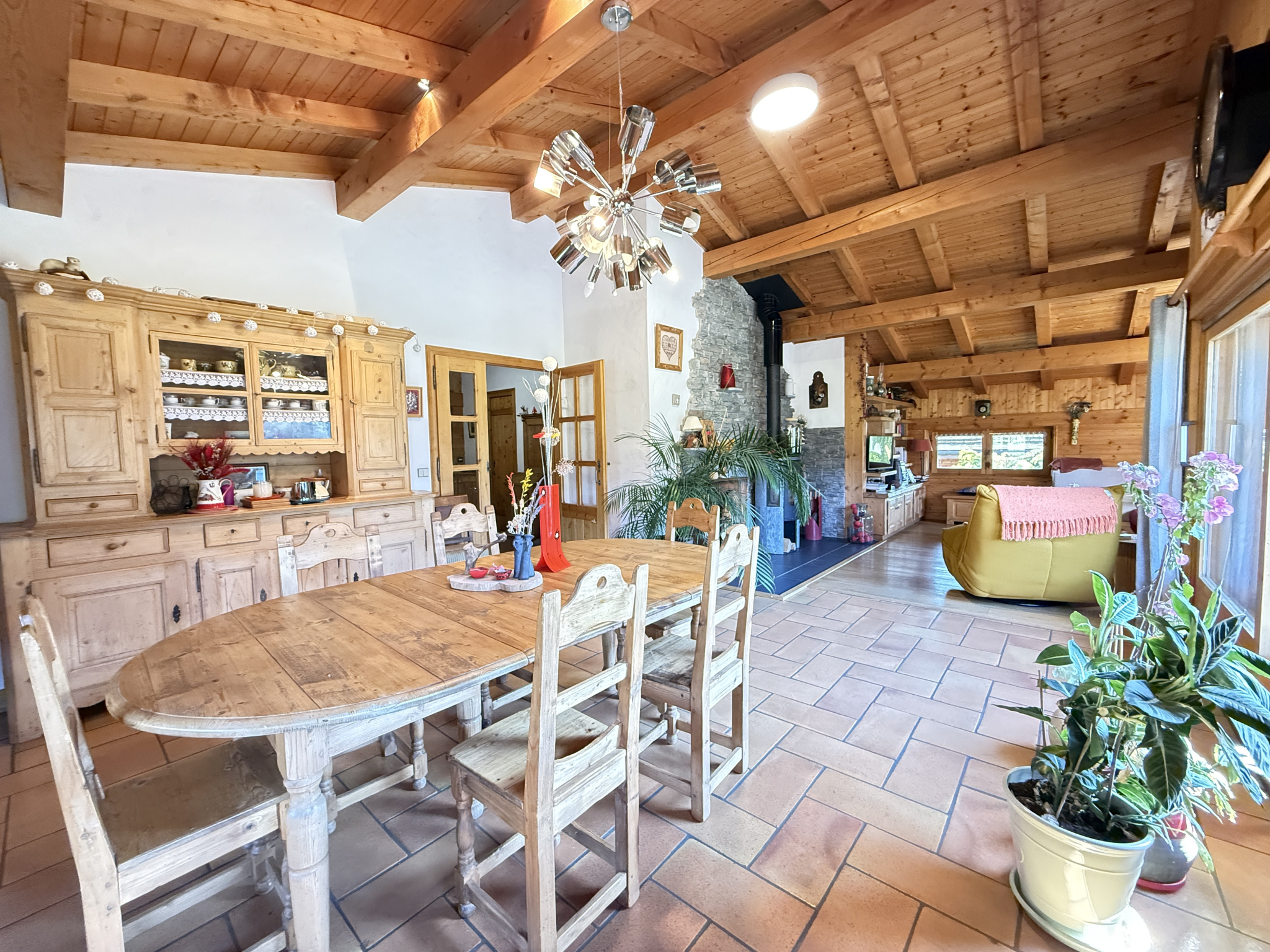 Interior of a traditional chalet with a large wooden table, chairs and a warm living space.