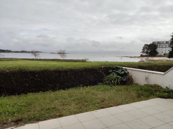 Vue sur la mer depuis un jardin privatif à Carnac, avec pelouse et plage en arrière-plan.