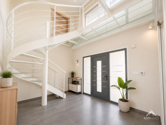 Intérieur d'une maison moderne avec un escalier en colimaçon et une entrée lumineuse.