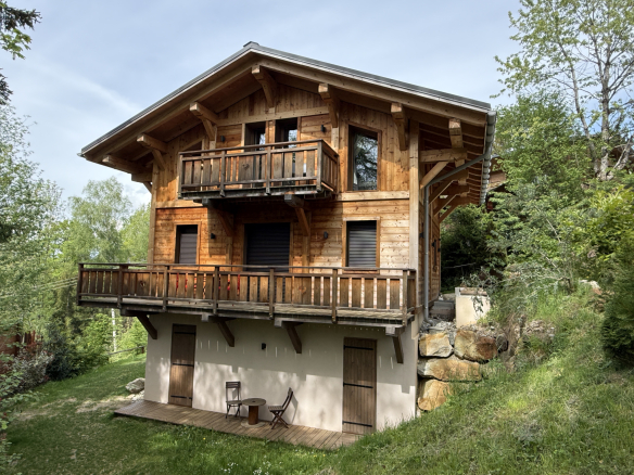 Alpine wooden chalet with balcony, located in Combloux, surrounded by greenery.