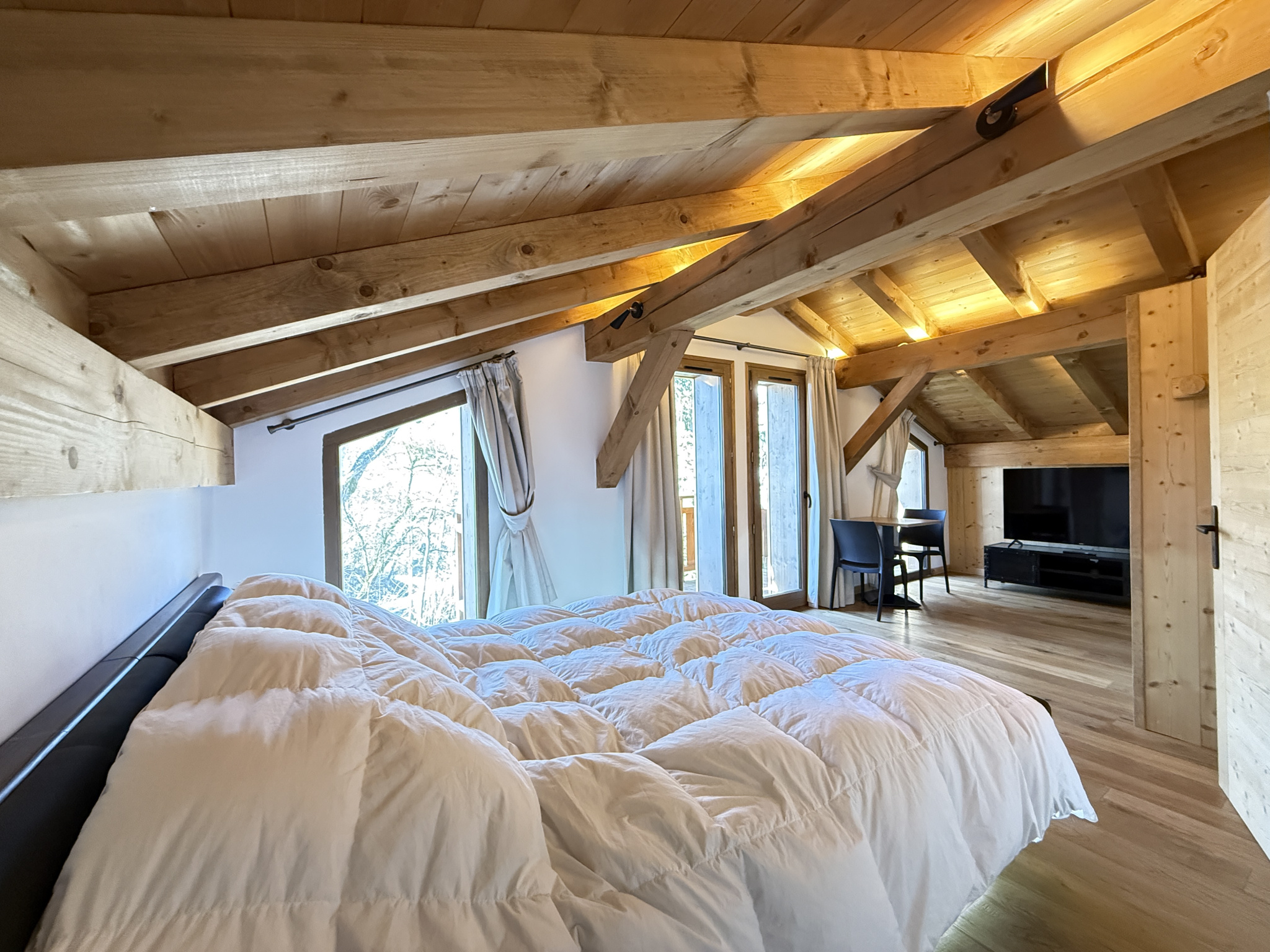 Alpine chalet in Combloux Interior of an alpine chalet with wooden beams and a double bed, windows overlooking nature.
