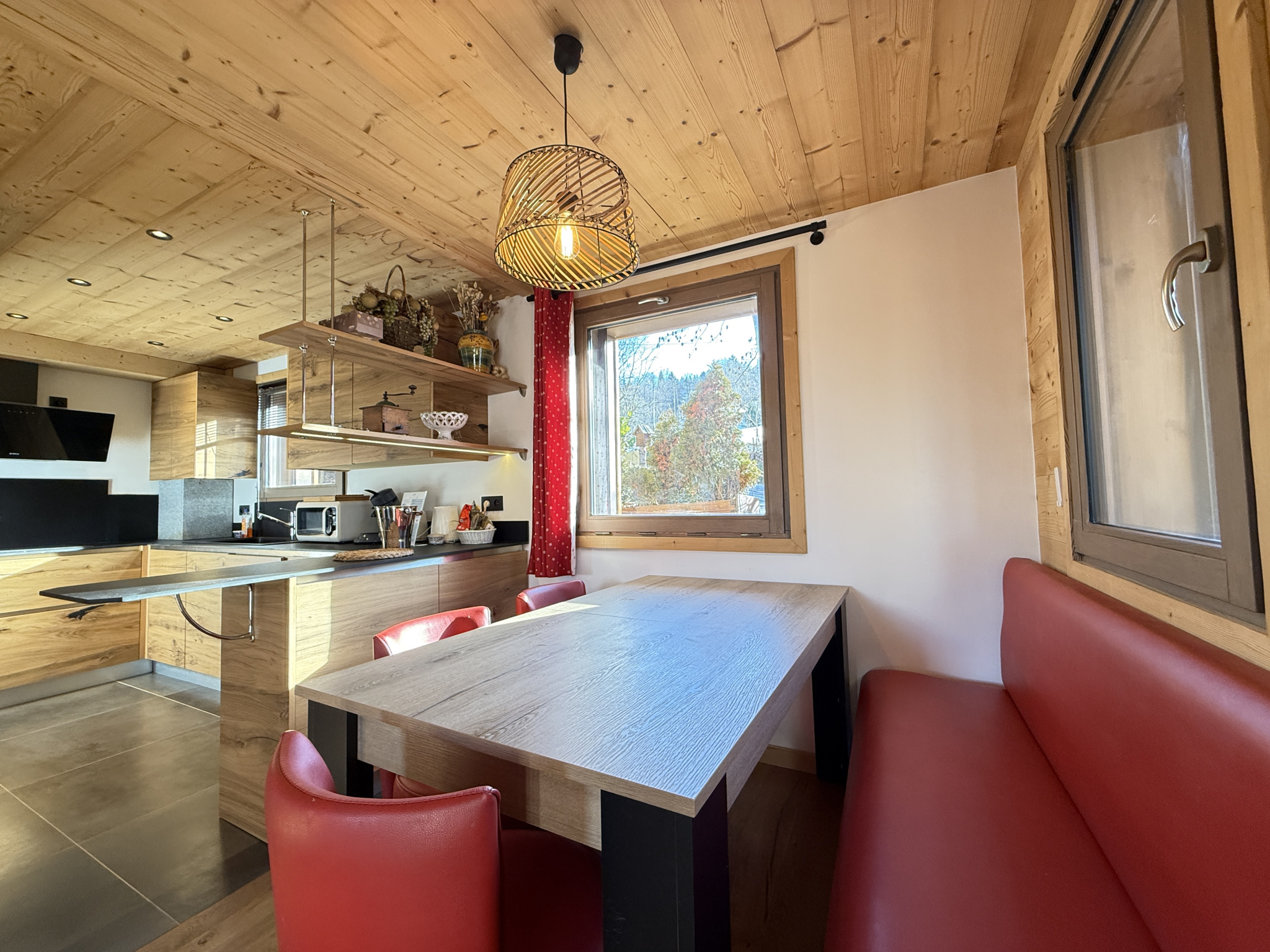 Interior of a chalet in Combloux Interior of an alpine chalet with a wooden table and red chairs, view of nature through a window.