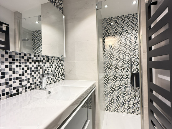 Modern bathroom with shower and sink, black and white tiles.