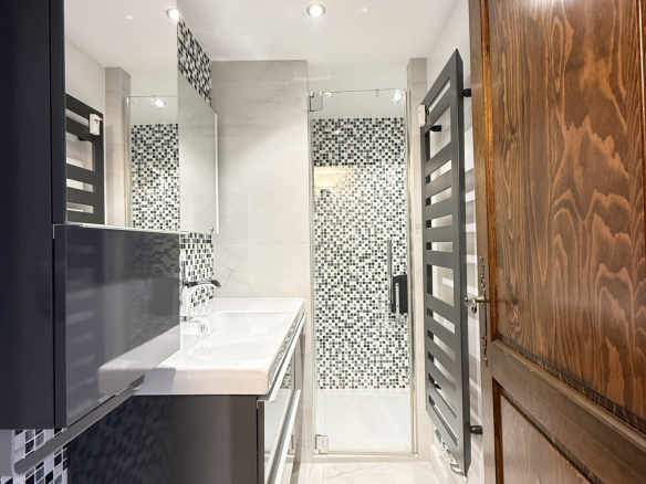 Salle de bain moderne avec carrelage noir et blanc, douche vitrée et meuble lavabo.