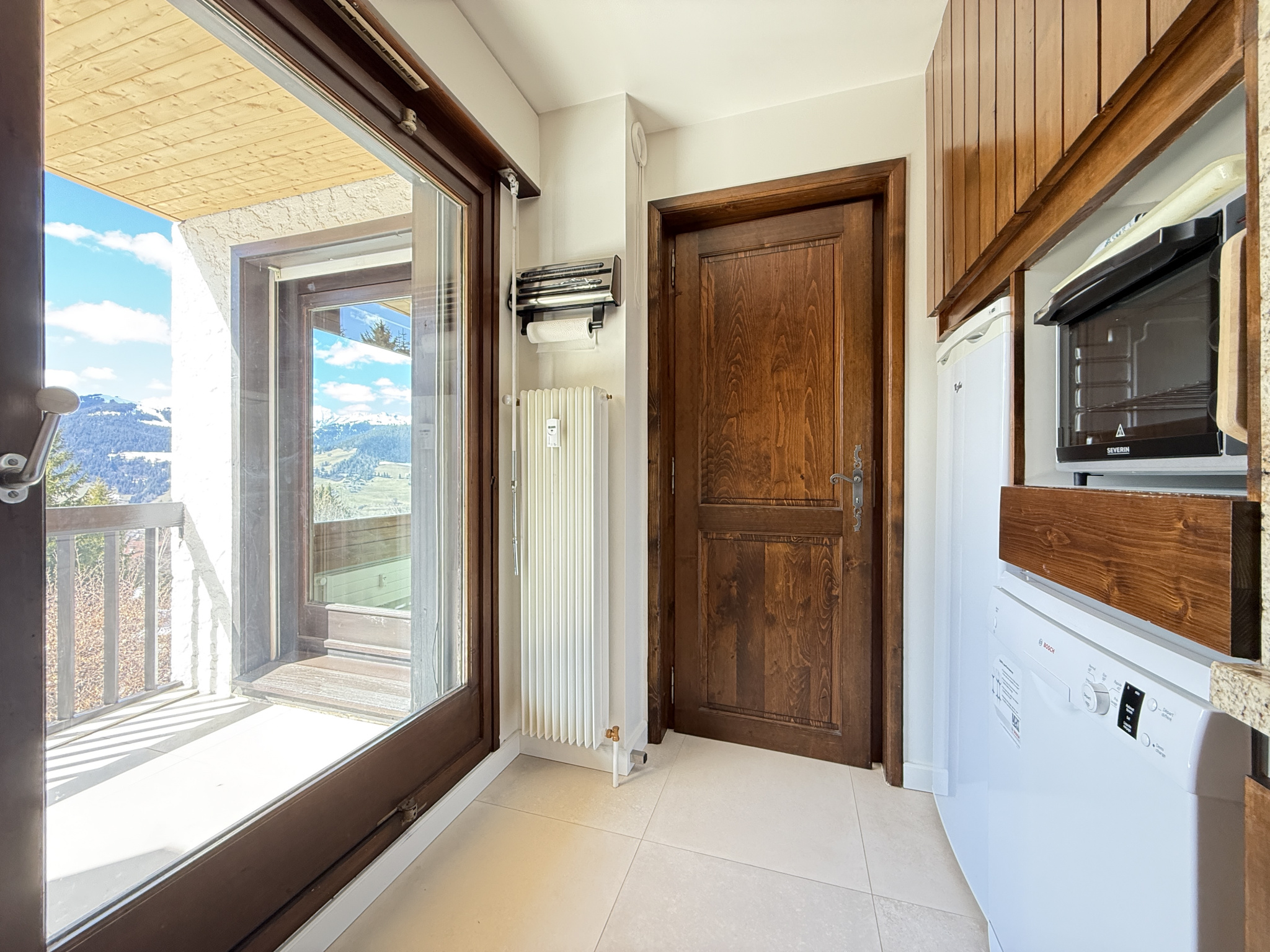 Intérieur d’un appartement à Megève Intérieur d'un appartement avec cuisine et accès à un balcon, vue sur les montagnes.
