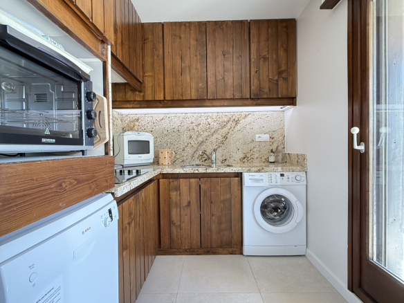 Cuisine équipée en bois dans un appartement à Megève, avec lave-linge et vue sur l'extérieur.