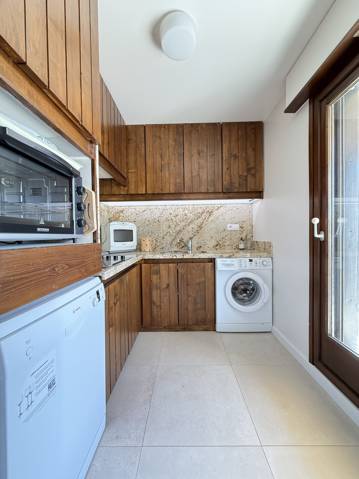 Cuisine de l’appartement Les Mandarines à Megève Cuisine équipée en bois dans un appartement à Megève, avec lave-linge et vue sur l'extérieur.