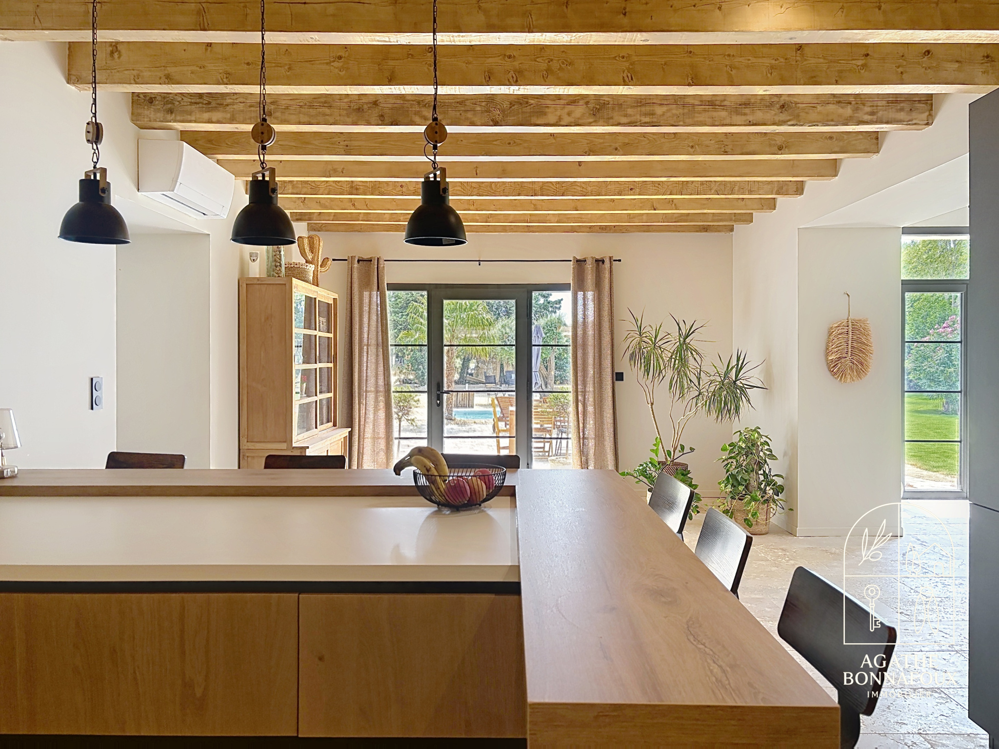 Interior of a renovated Provençal farmhouse with exposed beams and open kitchen/living room.