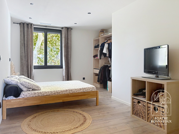 Room in a renovated Provençal farmhouse with wooden bed, open wardrobe and television.