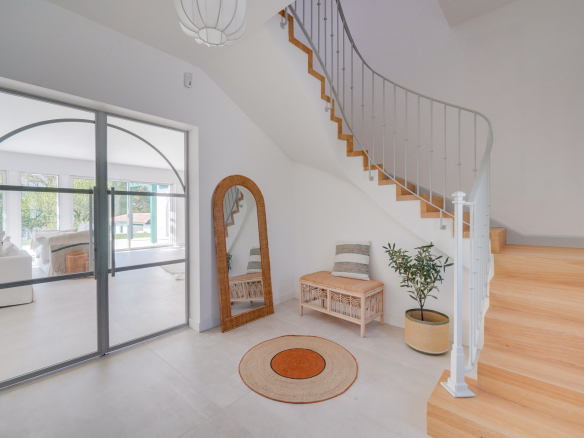 Intérieur d'une maison moderne avec un escalier en bois et un miroir, éclairage naturel.