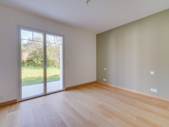 Intérieur d'une maison rénovée avec un sol en bois et des fenêtres donnant sur un jardin.