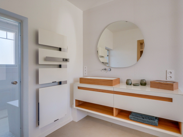 Salle de bain moderne avec meuble en bois et miroir ovale.