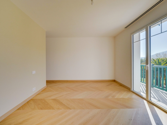 Intérieur d'une pièce vide avec parquet en bois et grandes fenêtres donnant sur un balcon.