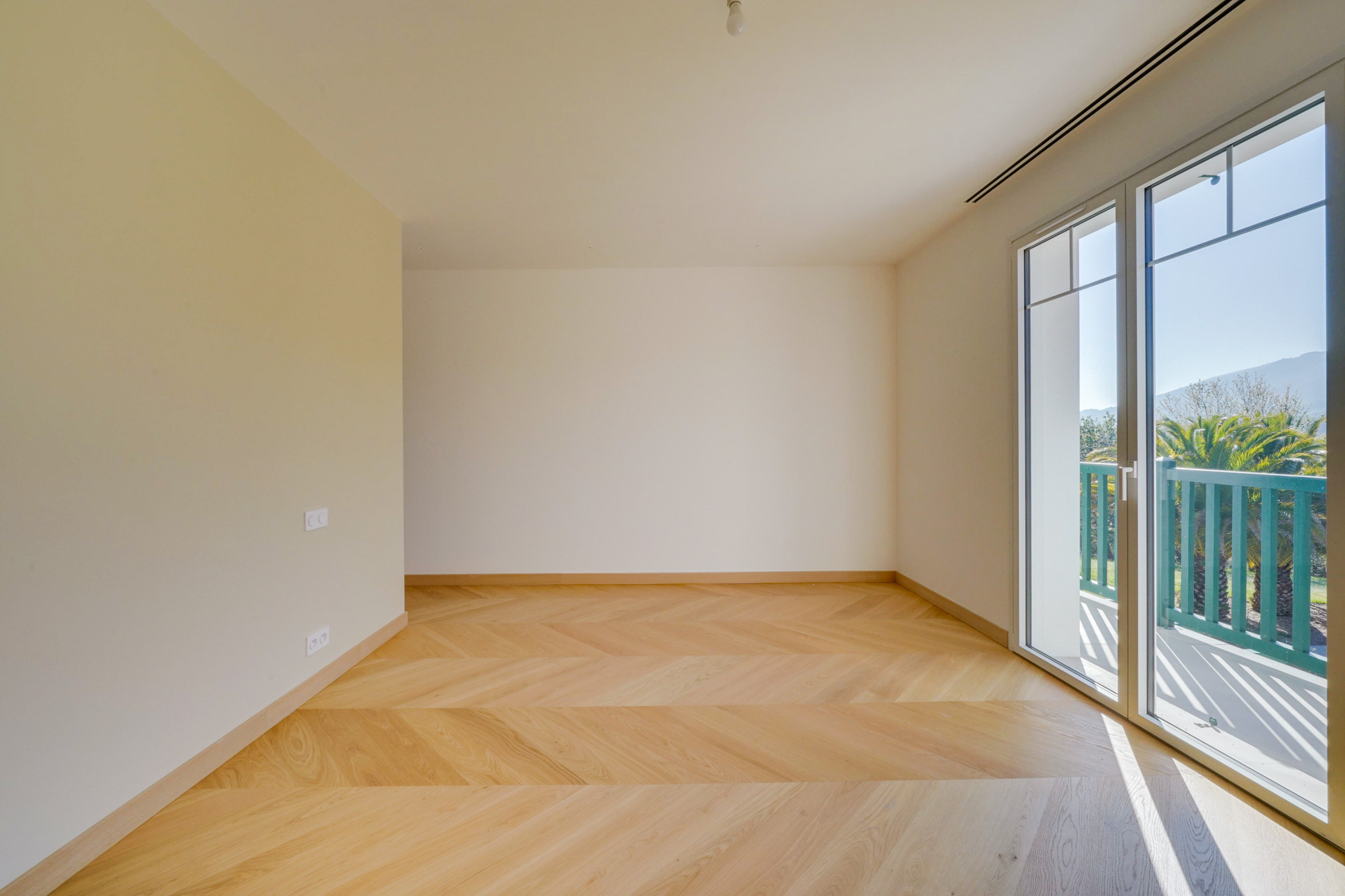 Intérieur d’une maison à Urrugne Intérieur d'une pièce vide avec parquet en bois et grandes fenêtres donnant sur un balcon.