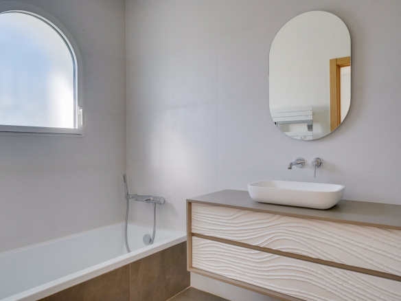Salle de bain moderne avec baignoire, miroir ovale et meuble sous lavabo.