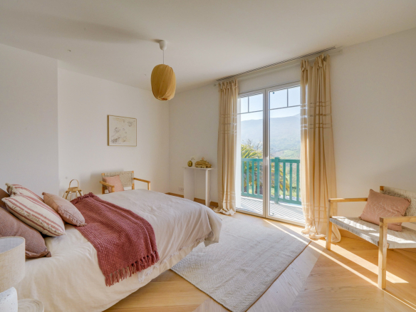 Chambre lumineuse avec lit double et accès à un balcon, vue sur la montagne.