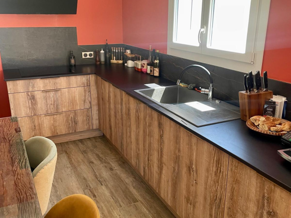 Modern kitchen with wooden furniture and red wall, equipped for meal preparation.