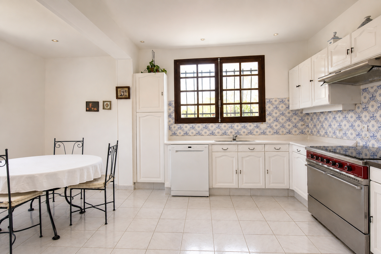 Spacious kitchen in Gradignan Bright kitchen with table and chairs, light-colored tiles, and small-paned windows.