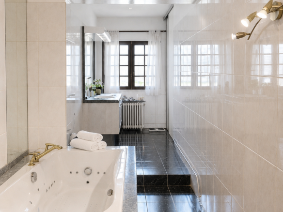 Modern bathroom with bathtub, black and white tiles, and windows letting in light.
