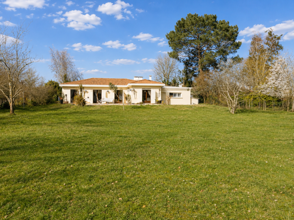 Single-storey house in Gradignan on a wooded plot with swimming pool, blue sky and clouds.