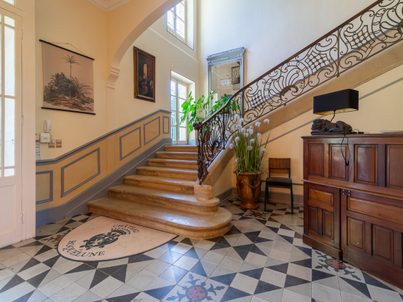 Interior of a castle with a stone staircase and a mosaic floor, decorated with plants and paintings.