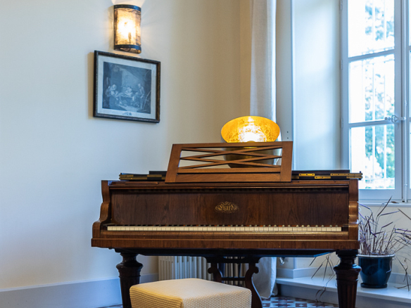 Antique piano in a room with decorative tiled floor and bright windows.