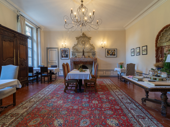 Interior of a castle with a large dining table, chairs, a rug and an ornate fireplace.
