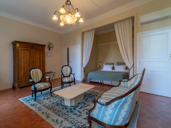 Interior of an elegant living room in a castle, with armchairs, a coffee table and a bed in the background.