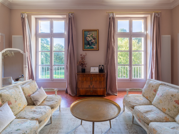 Interior of an elegant living room with two sofas, a coffee table and large windows overlooking a park.