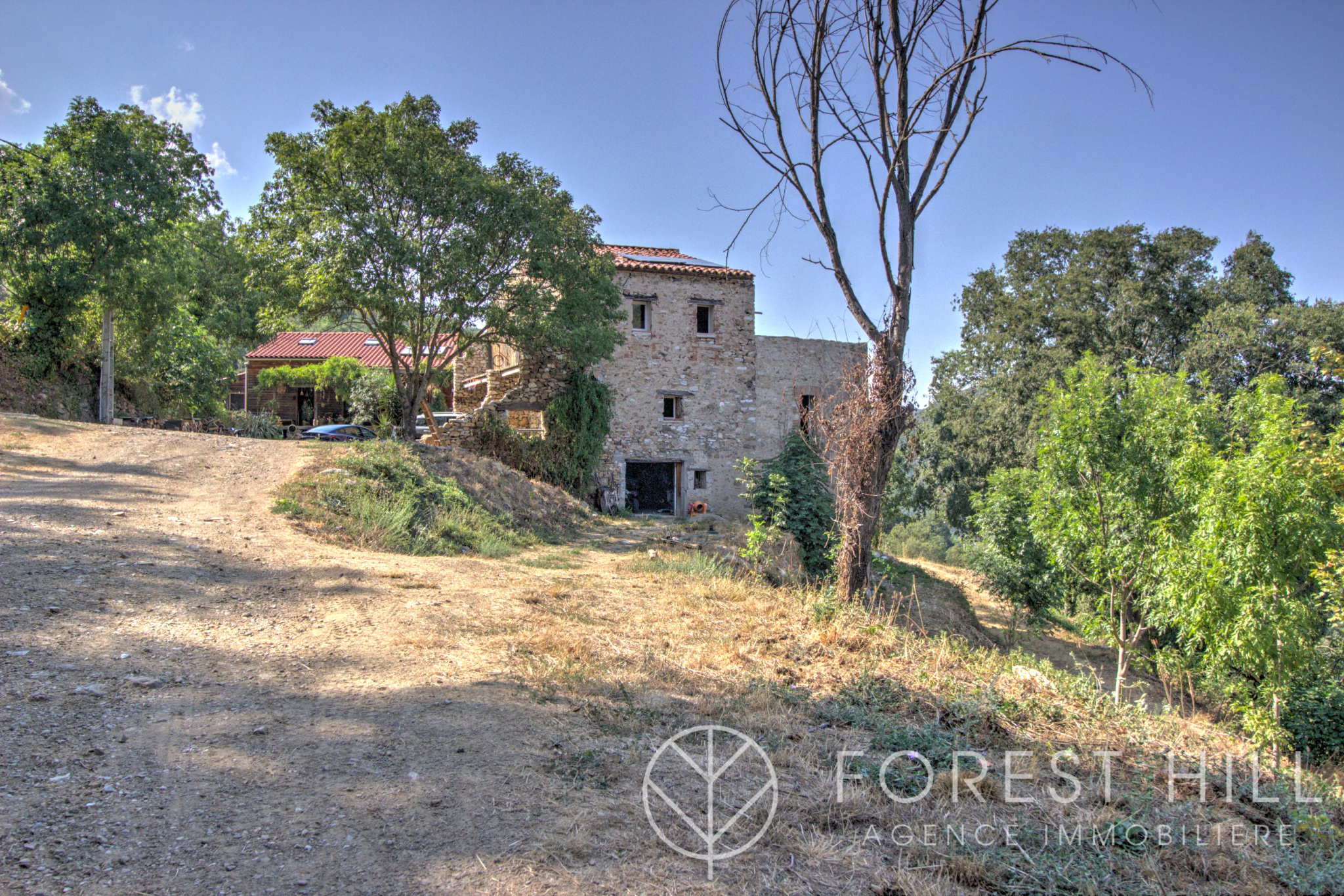 Stone property surrounded by nature in Montbolo, with access road and trees.