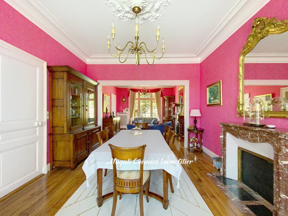 Intérieur d'une maison de maître avec murs roses, table à manger et cheminée en pierre.