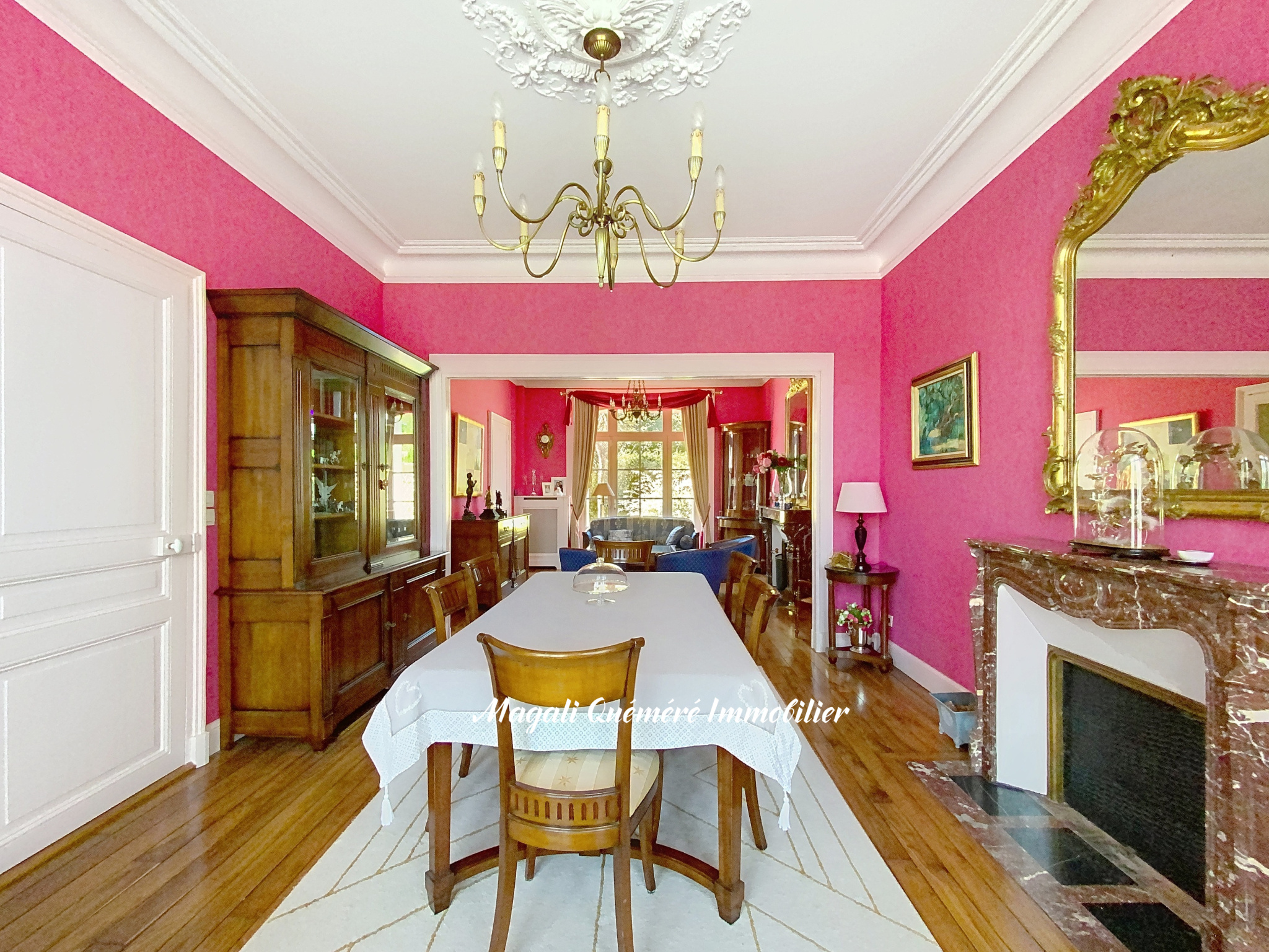 Intérieur d'une maison de maître avec murs roses, table à manger et cheminée en pierre.