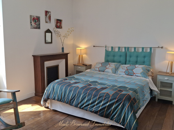 Chambre d'une maison rénovée à Ustaritz avec lit, fauteuil et cheminée.