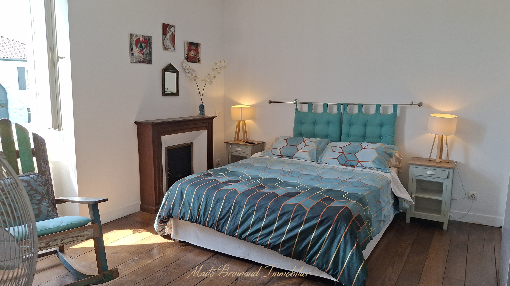 Chambre d'une maison rénovée à Ustaritz avec lit, fauteuil et cheminée.