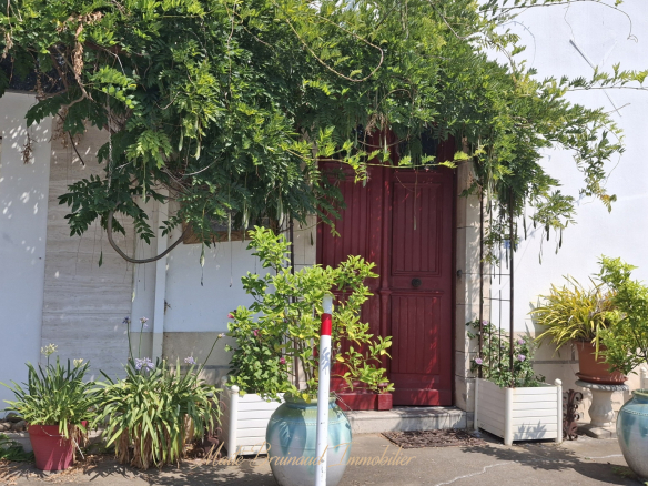 Entrée d'une maison de caractère à Ustaritz, avec une porte rouge et des plantes devant.