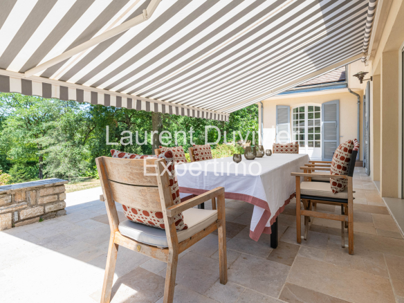 Terrasse d'une propriété à Auffargis avec table et chaises, entourée de verdure.