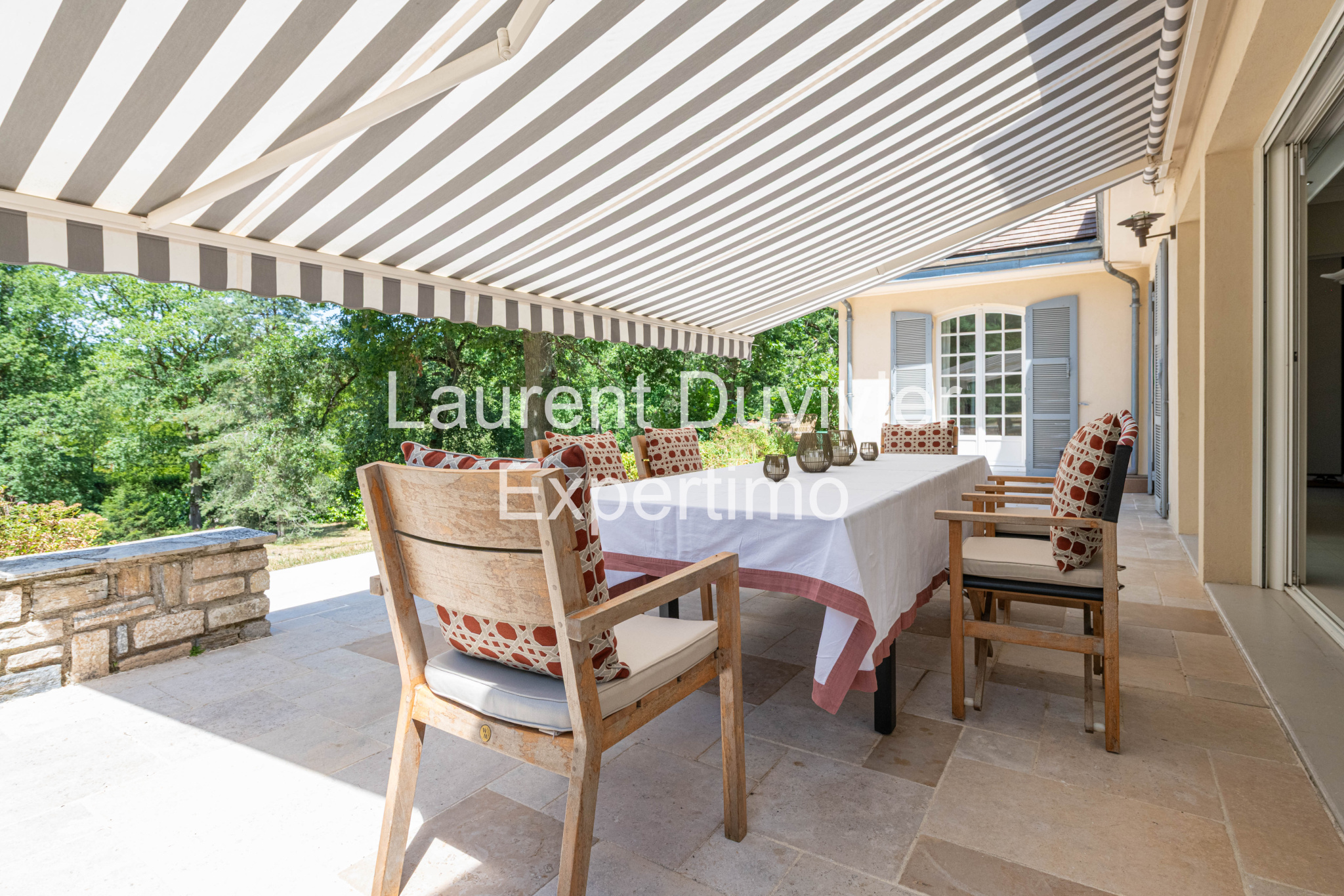 Terrasse d'une propriété à Auffargis avec table et chaises, entourée de verdure.