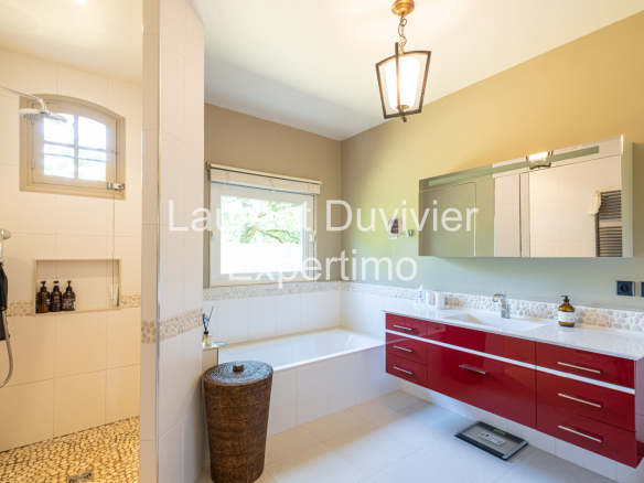 Salle de bain moderne avec douche et baignoire, murs clairs et meuble rouge à Auffargis.