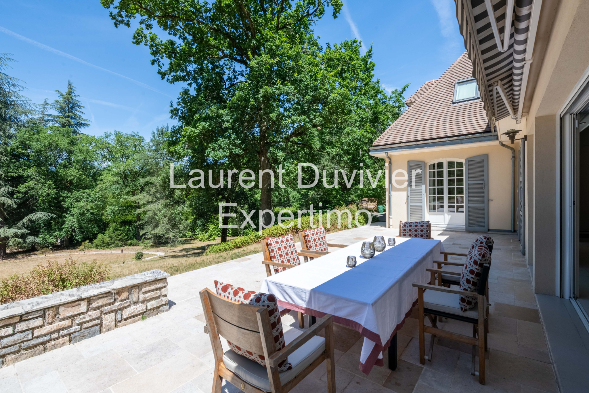 Terrasse d'une propriété à Auffargis avec une table et des chaises, entourée de verdure.