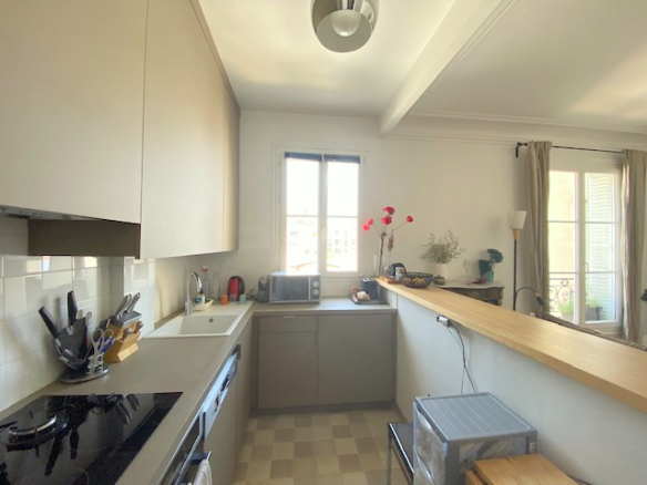 Cuisine moderne d'un appartement 3 pièces à Paris 12ème, avec fenêtres et plan de travail en bois.