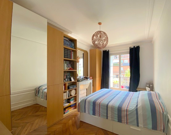 Chambre d'un appartement ancien à Paris 12ème, avec lit double et bibliothèque intégrée.