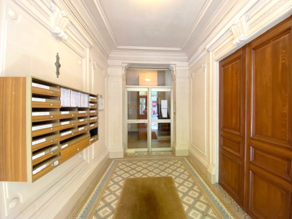Hall d'entrée d'un immeuble ancien avec boîtes aux lettres et sol en carreaux de ciment.