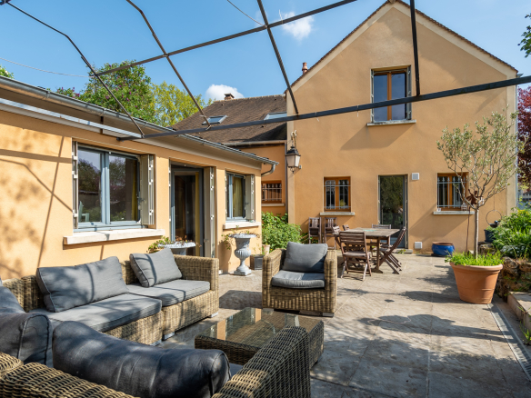 Terrasse d'une maison avec mobilier en osier, jardin verdoyant et façade jaune.