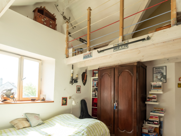 Chambre avec mezzanine, lit, bibliothèque et fenêtre lumineuse.