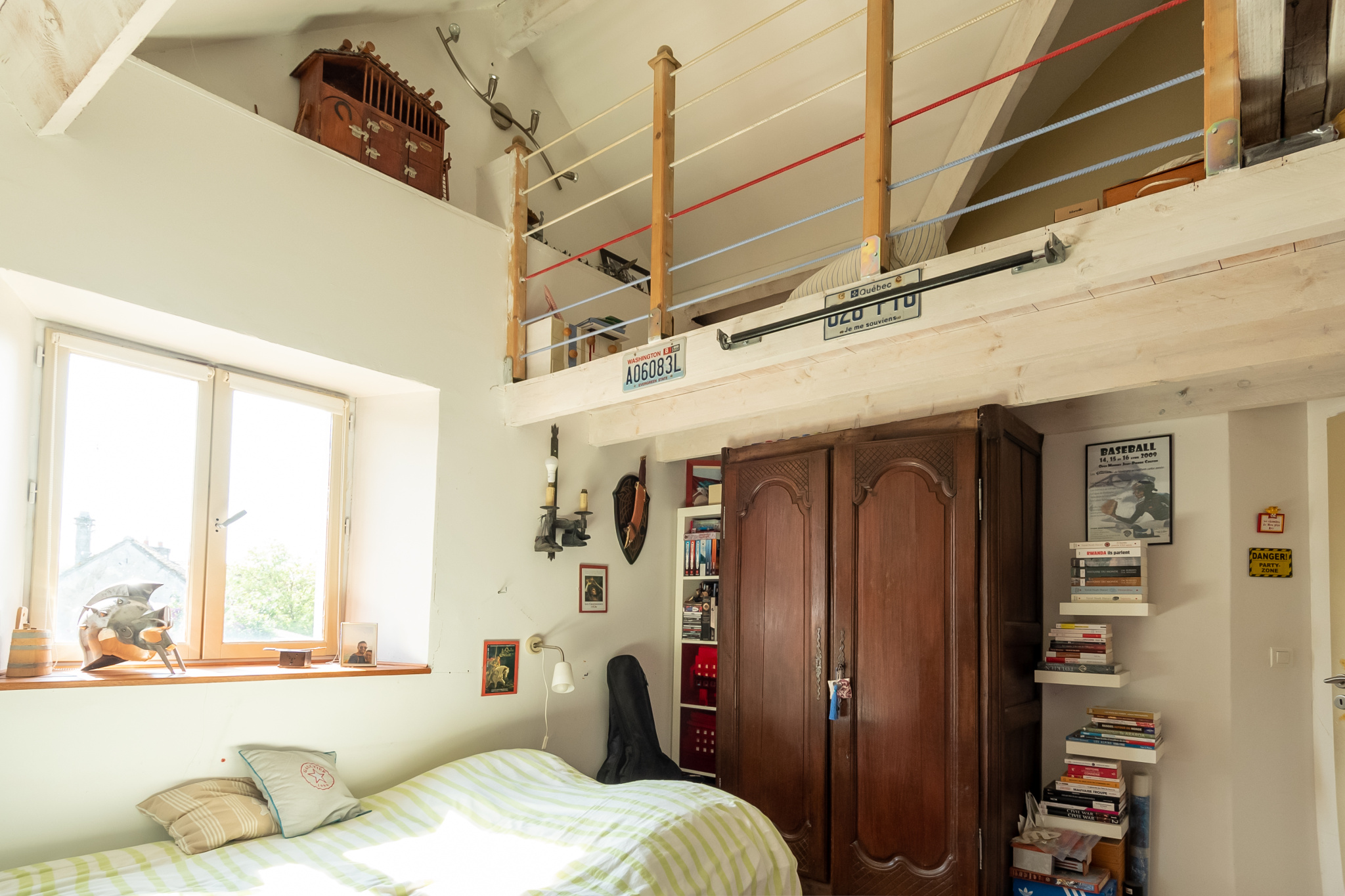 Chambre avec mezzanine, lit, bibliothèque et fenêtre lumineuse.