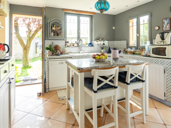 Cuisine lumineuse avec comptoir et chaises, vue sur le jardin, dans une maison de charme à Guyancourt.