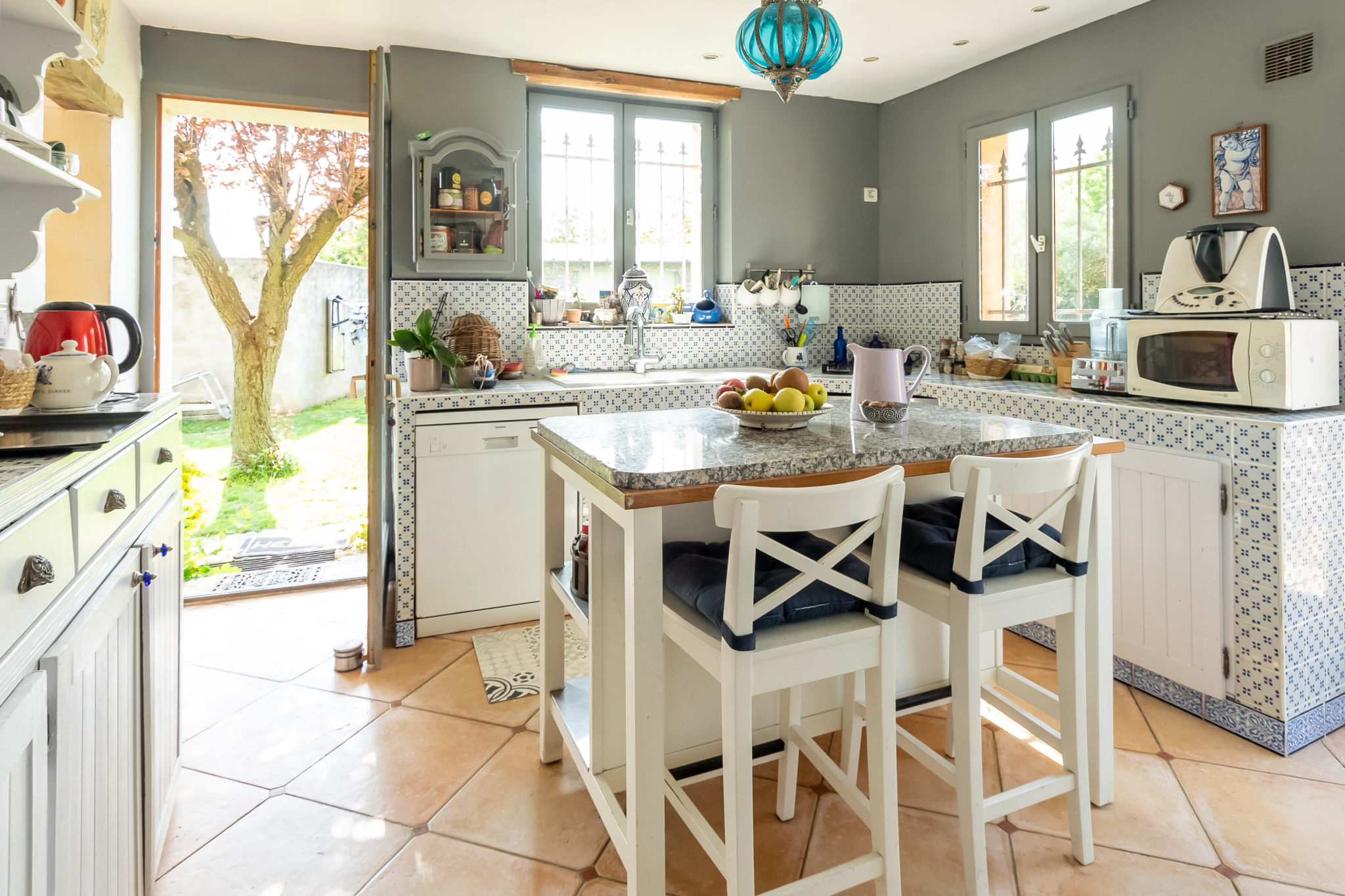 Cuisine lumineuse avec comptoir et chaises, vue sur le jardin, dans une maison de charme à Guyancourt.