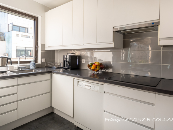 Cuisine moderne et lumineuse d'un appartement familial à Levallois-Perret, avec meubles blancs et plans de travail sombres.