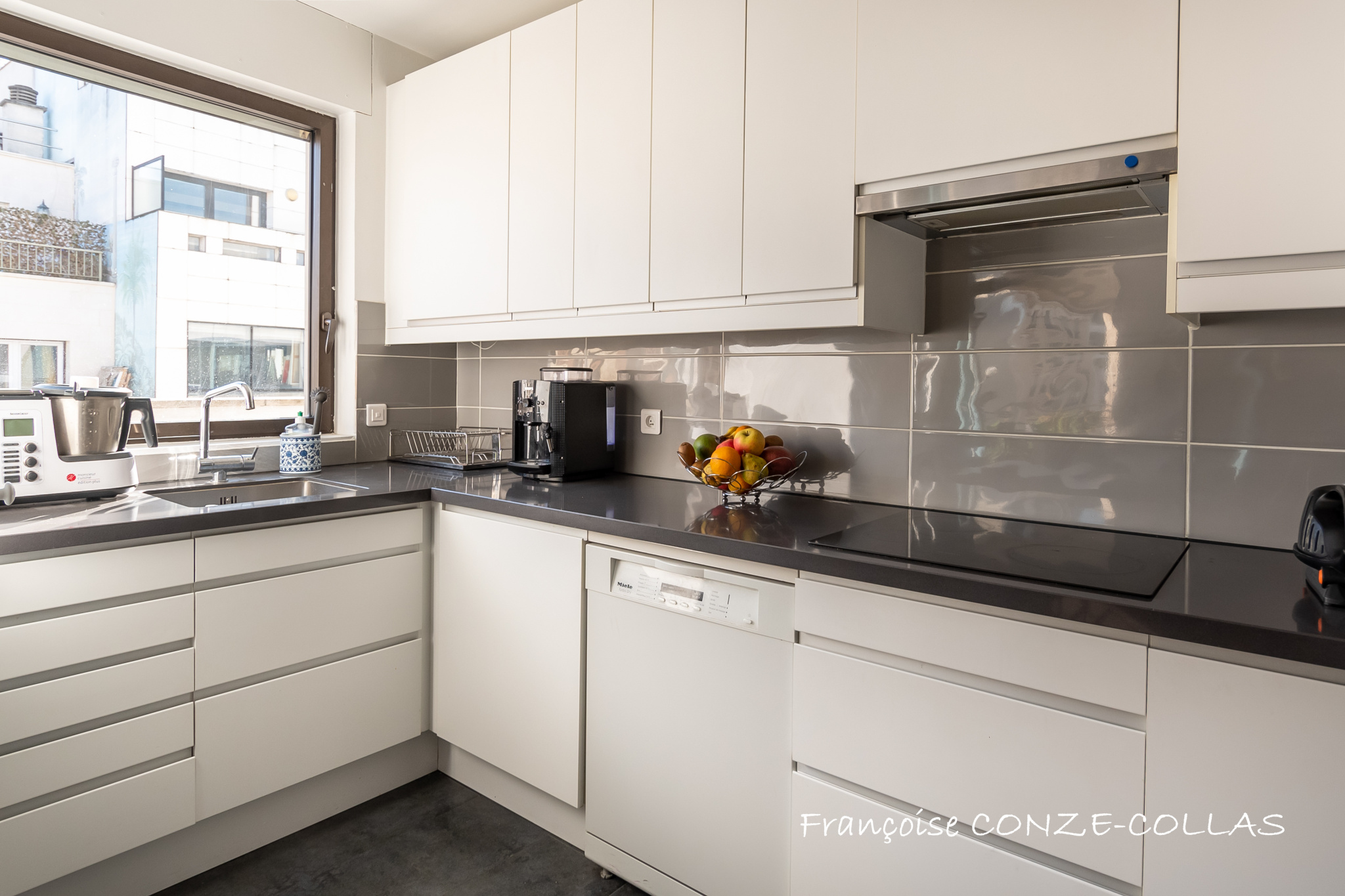 Cuisine moderne et lumineuse d'un appartement familial à Levallois-Perret, avec meubles blancs et plans de travail sombres.