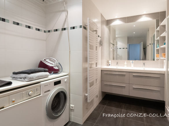 Salle de bain moderne avec machine à laver et lavabo, carrelage gris et murs blancs.
